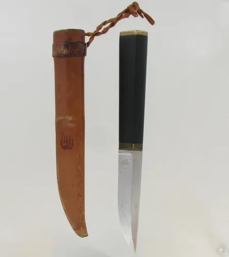 Puukko, design Tapio wirkkala, ruostumatonta terästä, nailonia ja messinkiä, nahkatuppi, suunniteltu 1961, pituus 21,5cm