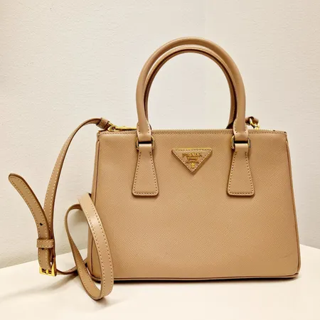 Käsilaukku Prada Saffiano Lux, väri Sand beige, pieniä likatahroja pinnassa ja kulumaa pohjanapeissa, irrotettava avaimenperä puuttuu, takuukortti, ostokuitti ja suojapussi.
